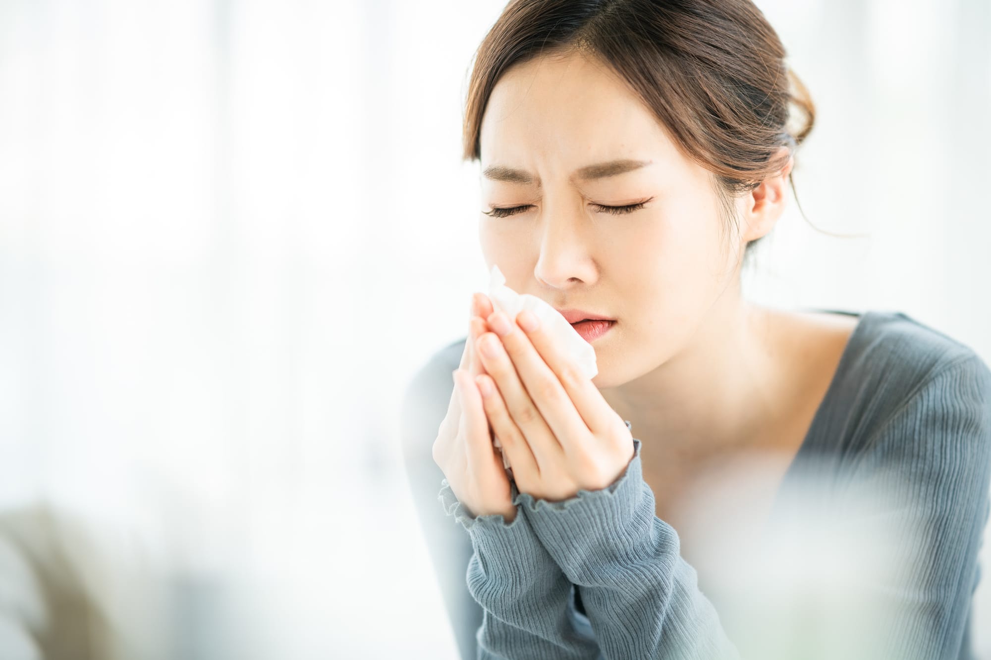 A Japanese woman suffering from hay fever holds a tissue close to her face as she closes her eyes in discomfort.