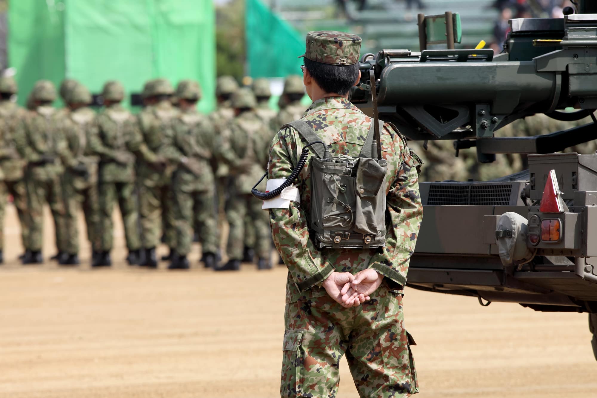 Japan Self Defense Force (JSDF) member at attention next to a tank.