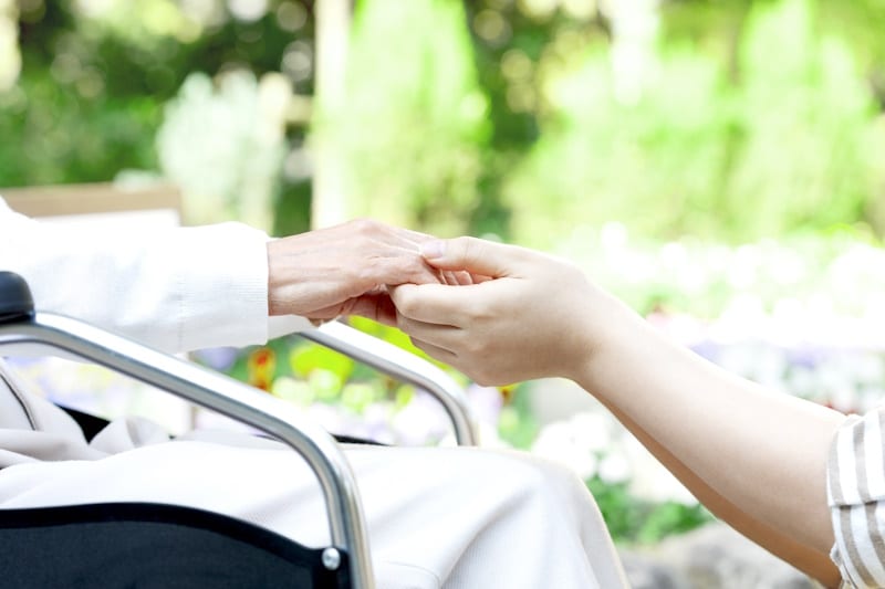 Nursing home - someone holding the hands of a woman in a wheelchair