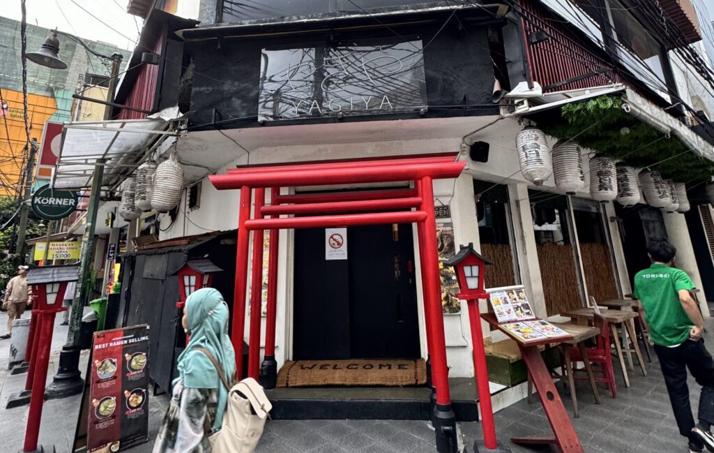 Small red torii gates lead into a Japanese restaurant in Jakarta's Little Tokyo, with woman in Indonesian tudong hair wrap walking in front.