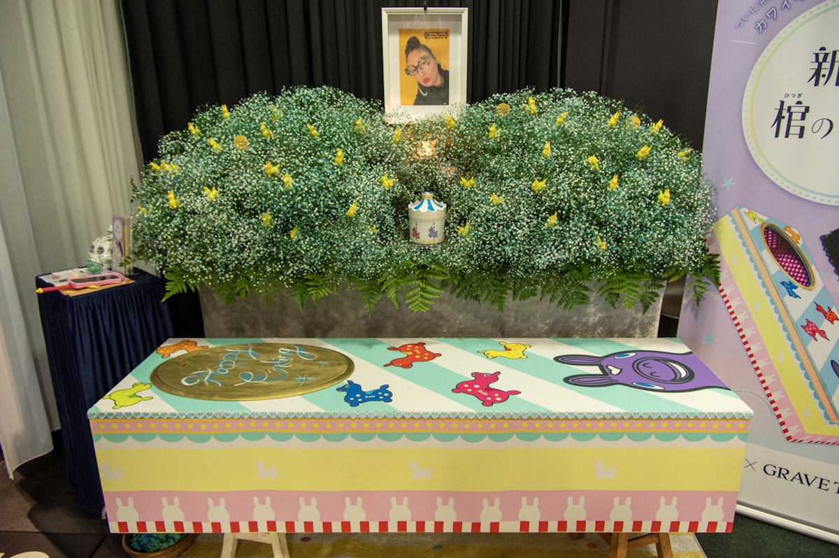 Colorful painted coffin with someone's pictured above it and flowers in the background